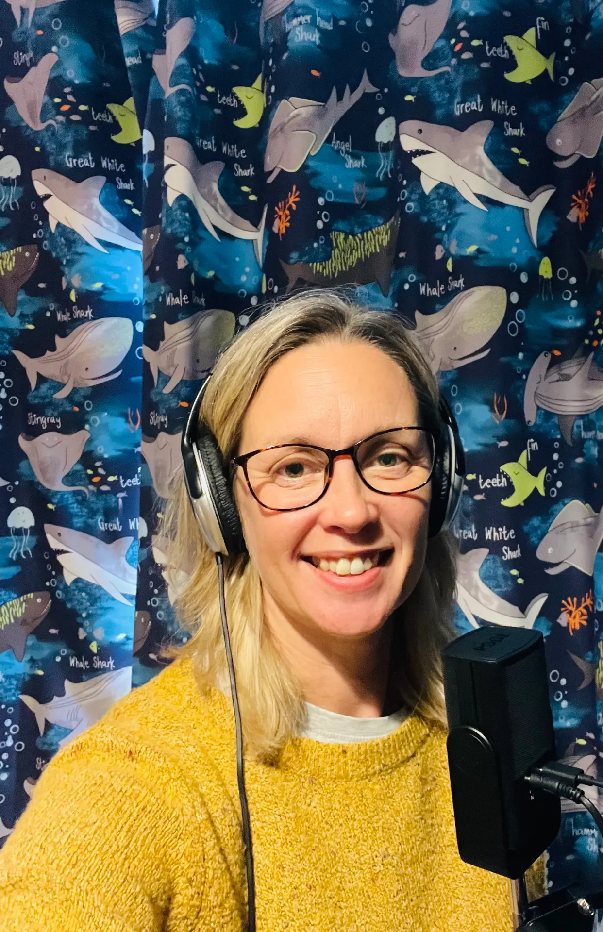 Susanna Fields, host of The Dream Tunnel Podcast, smiling in a yellow jumper with studio headphones